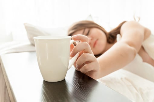 Closeup portrait of beautiful woman taking cup of coffee at bed