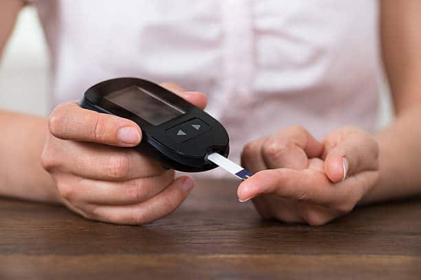 Close-up Of Person Hands Holding Glucometer At Desk