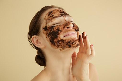 Woman exfoliating face with a coffee scrub, studio shot.