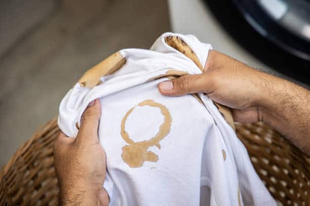 White cotton shirt A lot of stains, stains, coffee stains, man's hand holds the shirt up and spreads it to look dirty Must be brought to the washing machine