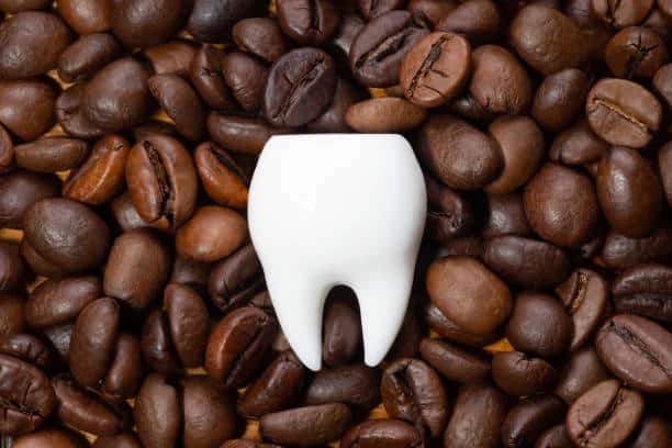 Large white tooth on a pile of roasted coffee beans. Coffee staining and teeth whitening concept.