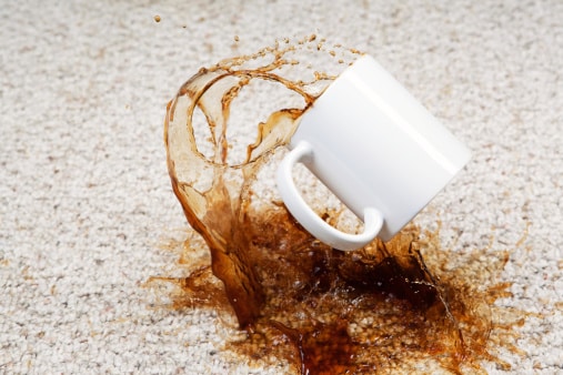 A coffee cup has fallen and coffee is splashing from the cup onto a clean carpet floor. Focus is on the cup which provides great copy space for a carpet cleaning business or other concept.