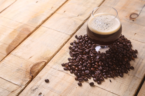Snifter glass with coffee stout surrounded by roasted coffee beans over a grunge wooden background