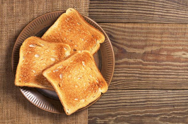 Slices of toasted bread in plate on wooden table, top view. Space for text