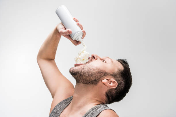 chubby man spraying whipped cream in mouth on white