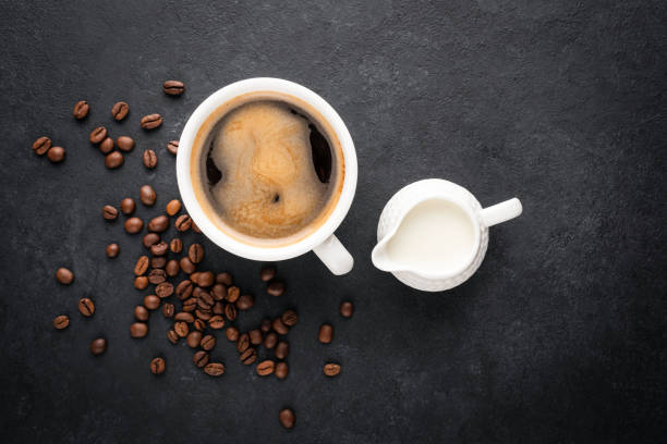 Cup of black coffee and coffee creamer in a jug on black concrete background, top view