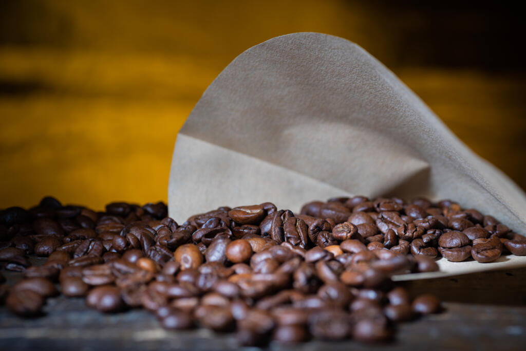 Coffee beans in a filter paper on a wooden table in front of a yellow lit background