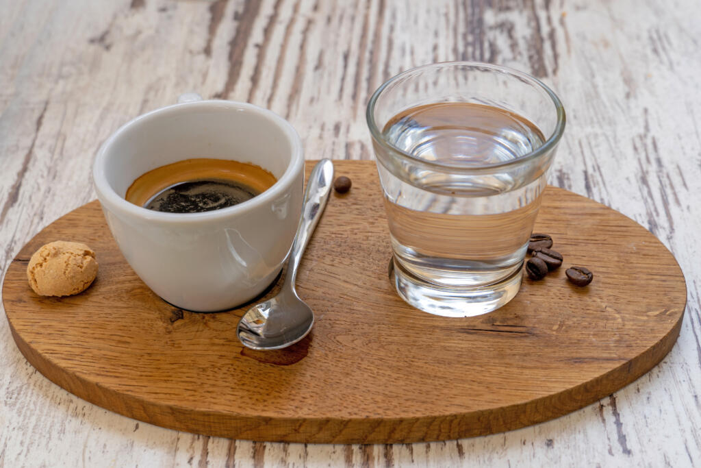 White cup of Espresso and a glass of water disposed on a wooden plate