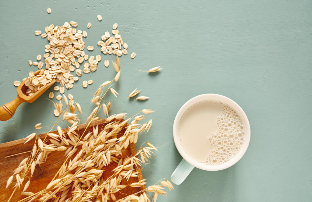 Oat milk in a glass and mug on a blue background. Flakes and ears for oatmeal and granola on a wooden plate.