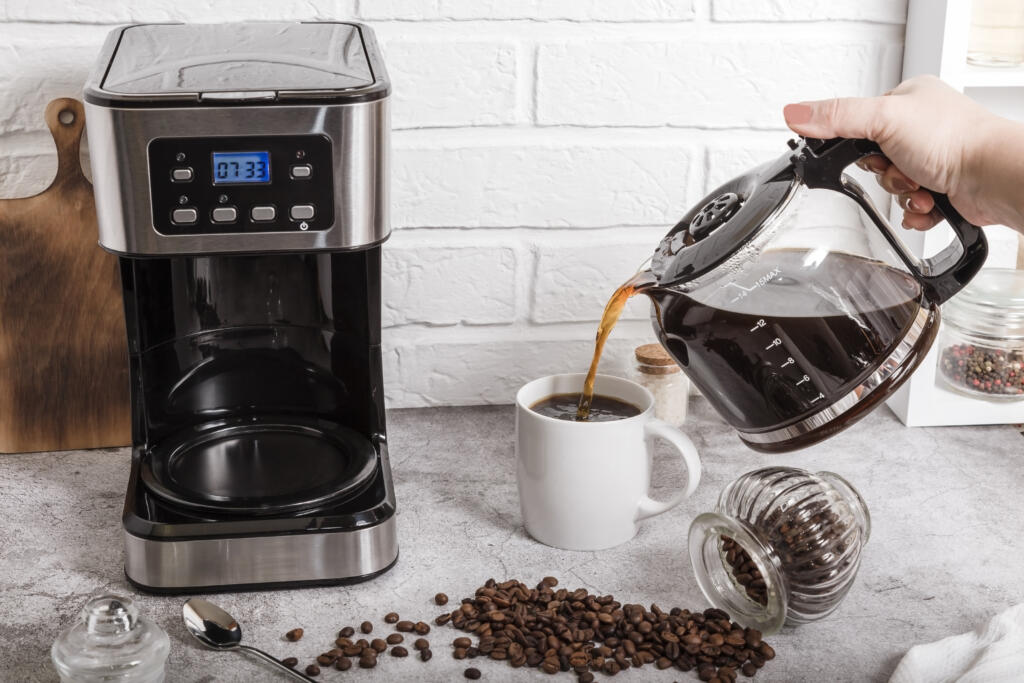 A woman's hand pours coffee from a coffee pot into a cup. Home life. Electric coffee maker on the kitchen countertop.