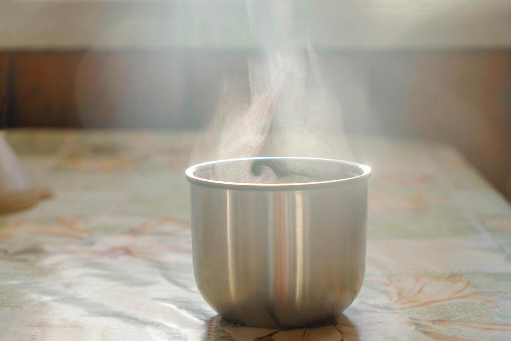 Isolated, metal thermos cup with tea or coffee on the table. The hot liquid evaporates. 