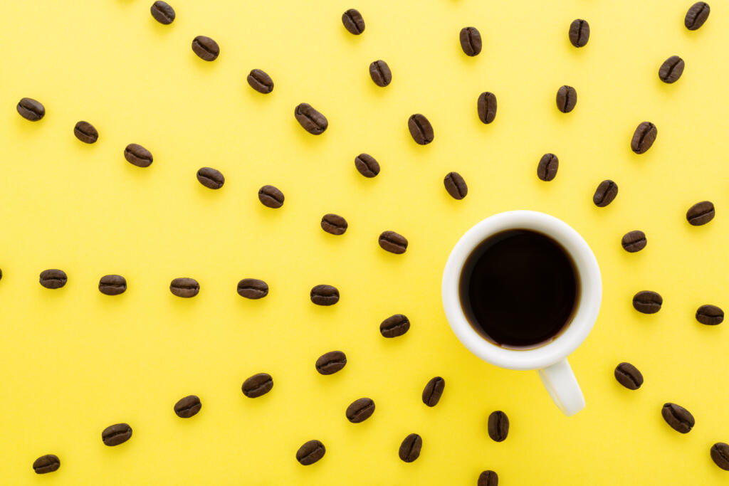 Cup of coffee espresso with sun rays of coffee beans on yellow background. Flat lay, creative design. Sunny morning & black coffee concept.