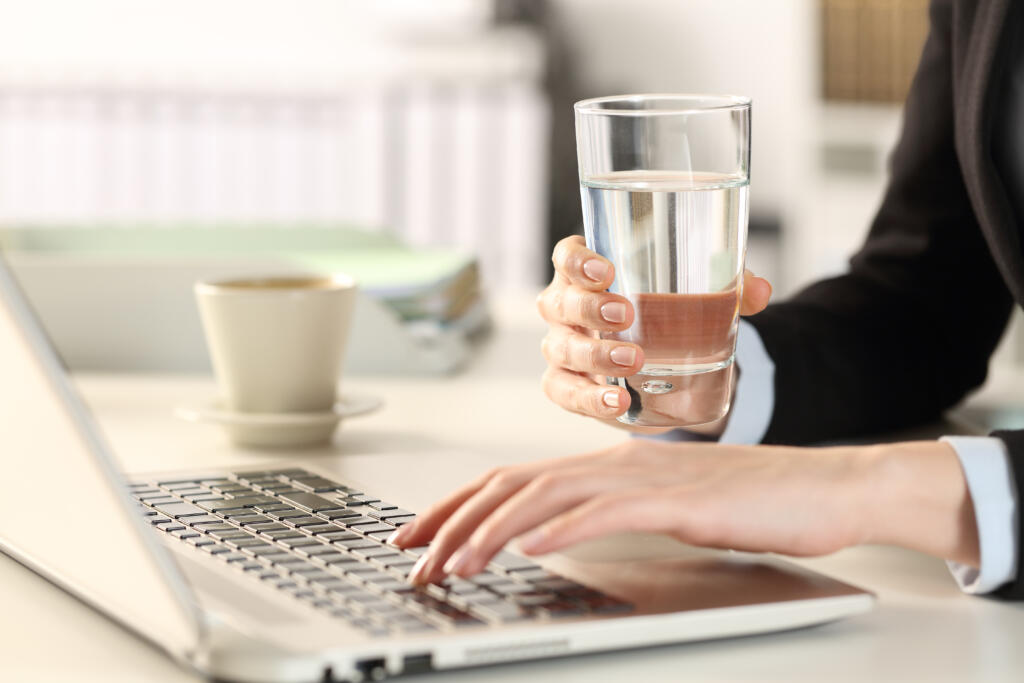 Executive hands holding water glass using laptop at office
